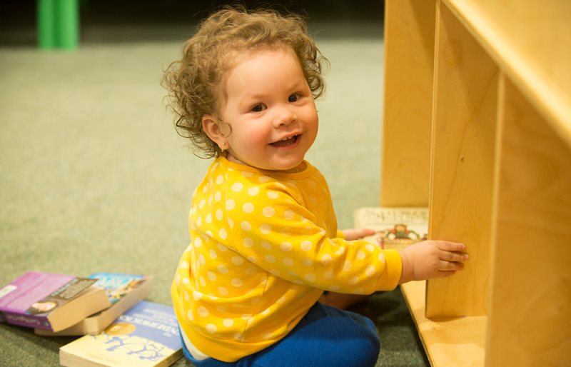 Smiling toddler playing with books at Family Resource Center at Texas Scottish Rite Hospital for Children