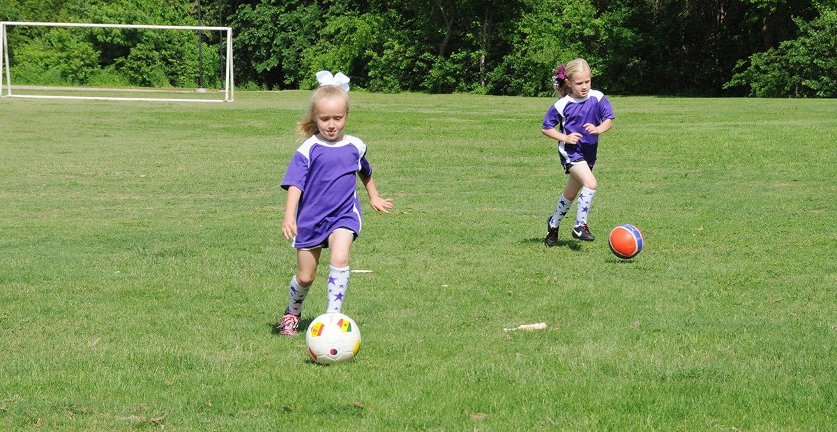 Two young girls playing soccer outside.