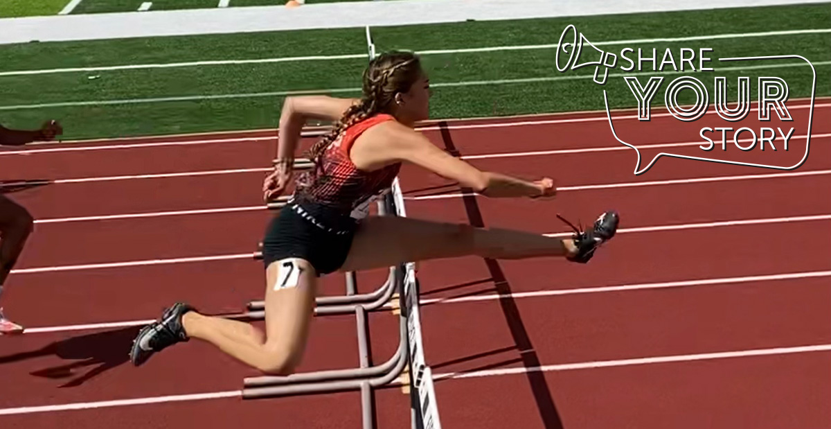 girl jumping over a hurdle on an outside track