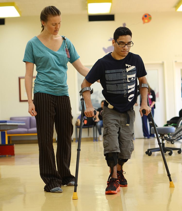 Physical therapist helping patient with forearm crutches walk at Texas Scottish Rite Hospital for Children