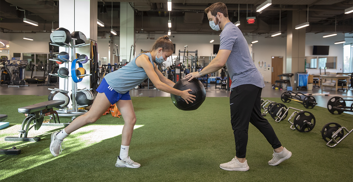 Athlete and trainer using a medicine ball in a gym.