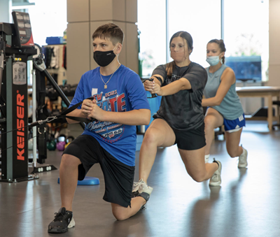 Three individuals performing resistance band exercises in a gym, all wearing masks.