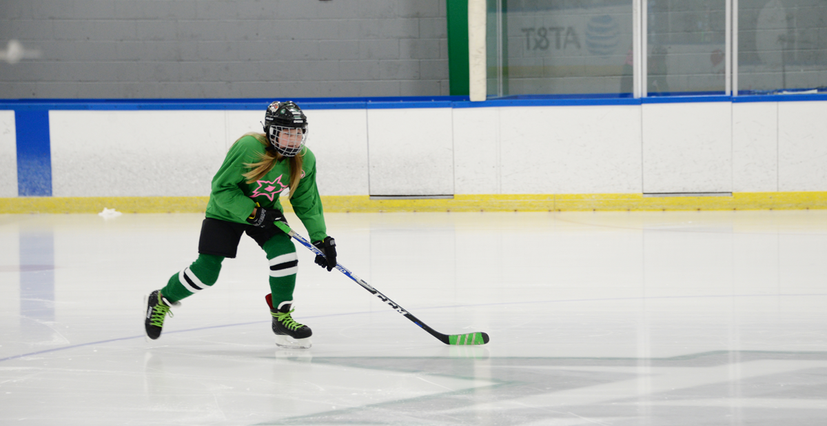 Female hockey player in green and black on ice rink.